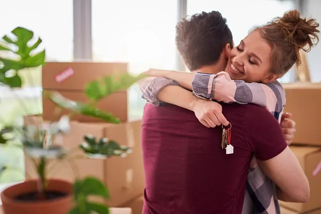Paar umarmt sich mit dem Schlüssel zur neuen Wohnung zwischen Umzugskartons